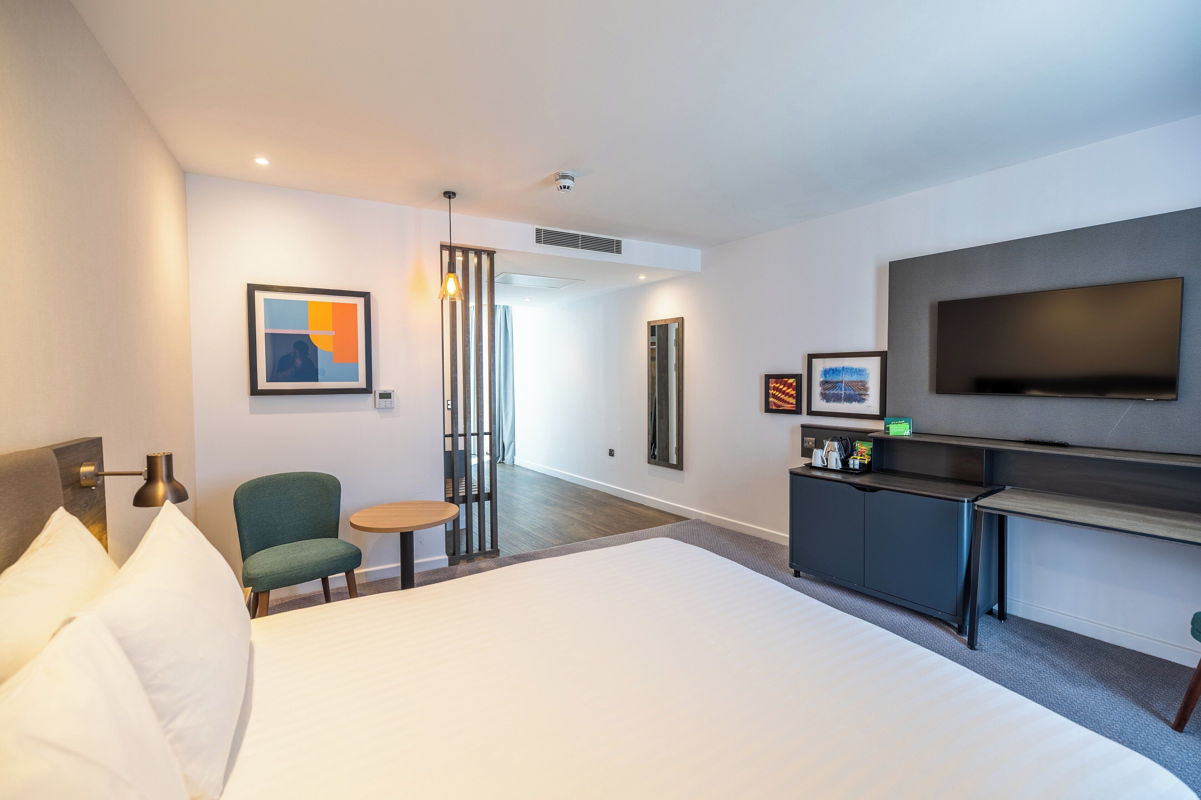 Una habitació d'hotel amb un llit gran, una televisió penjada a la paret, un escriptori amb una cadira i una taula petita.
