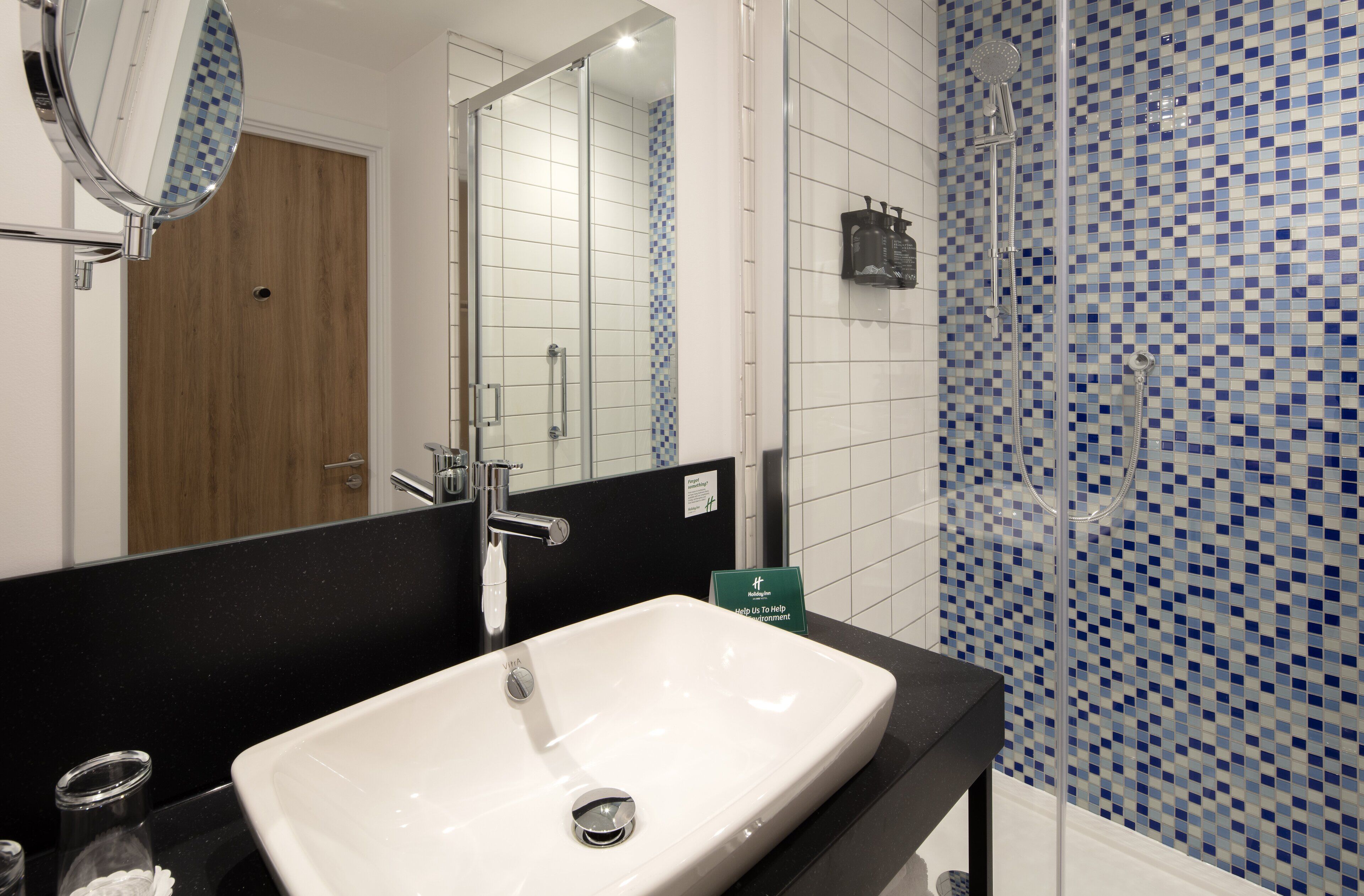 A bathroom with a white sink, a mirror, and a shower area with blue mosaic tiles.