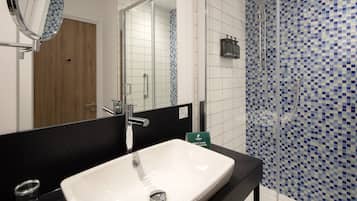 A bathroom with a white sink, a mirror, and a shower area with blue mosaic tiles.