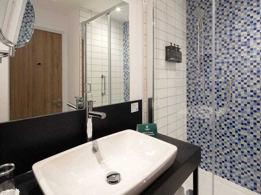 A bathroom with a white sink, a mirror, and a shower area with blue mosaic tiles.