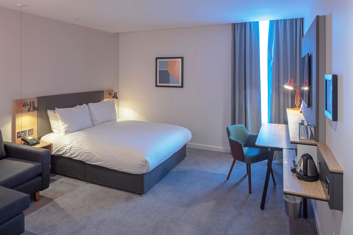 Une chambre d’hôtel avec un grand lit, un bureau avec une chaise, une télévision et une petite kitchenette.