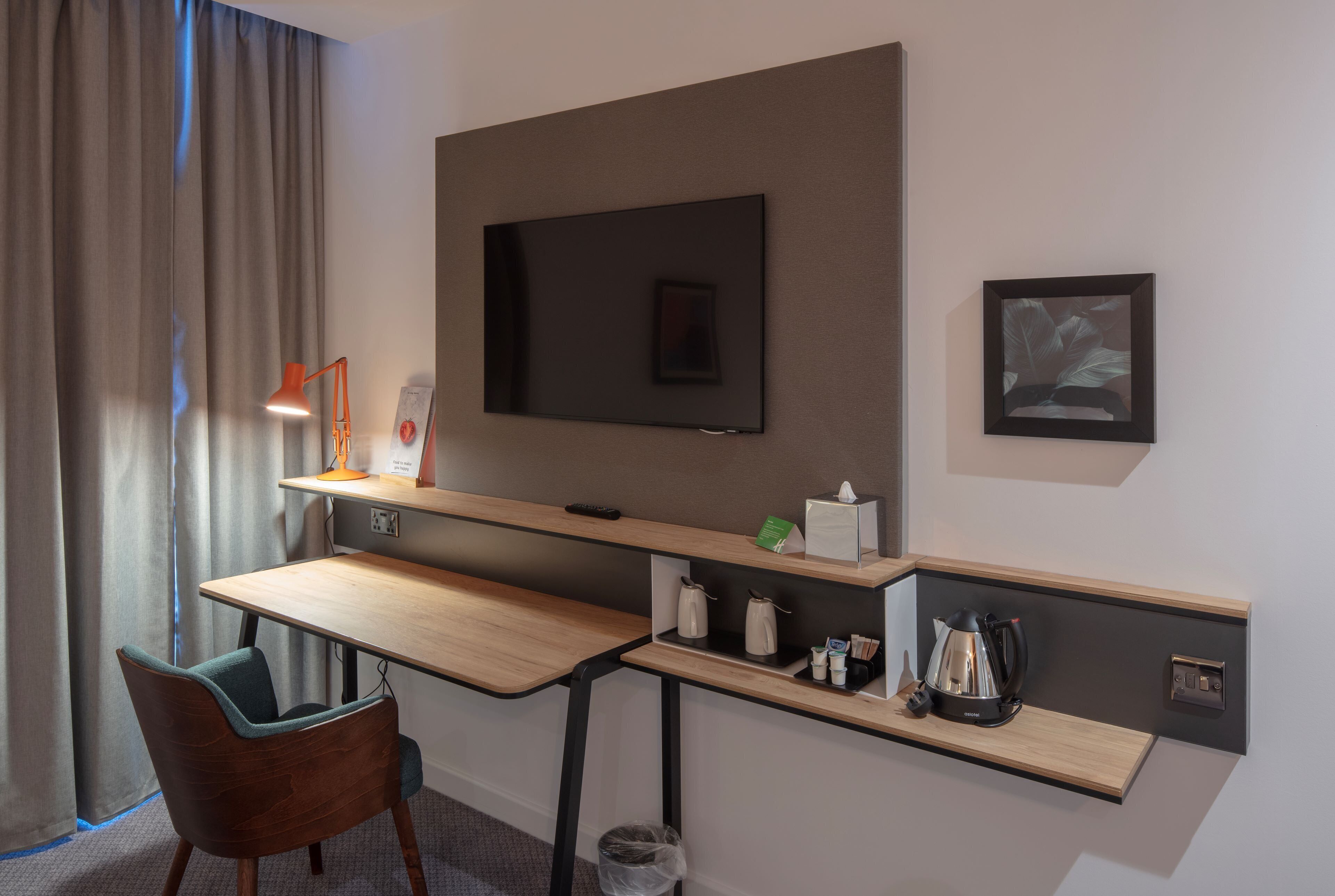 Ein Hotelzimmer mit Schreibtisch, Stuhl, Fernseher und einer kleinen Ablage für Annehmlichkeiten.