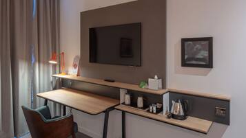 A hotel room with a desk, chair, television, and a small shelf with amenities.