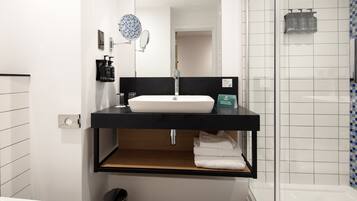 Un baño moderno con lavamanos blanco, encimera negra y cabina de ducha de vidrio.