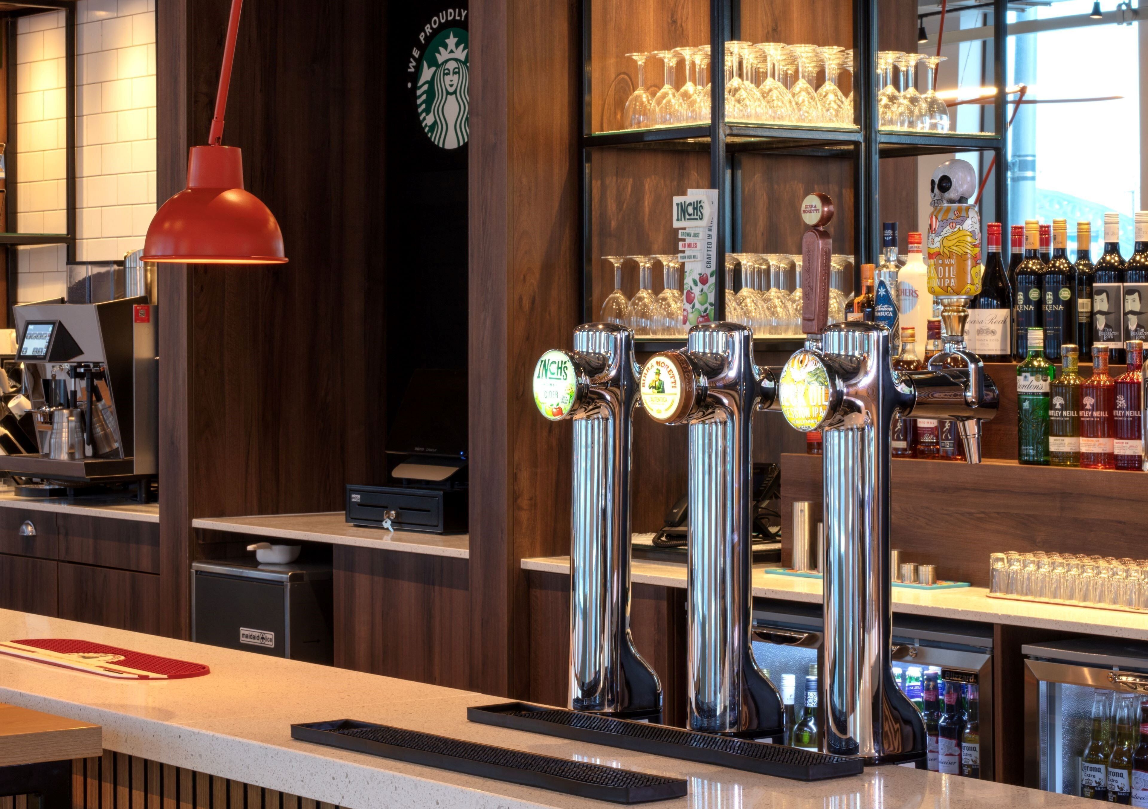 A bar area with multiple taps, a cash register, and shelves stocked with bottles and glasses.