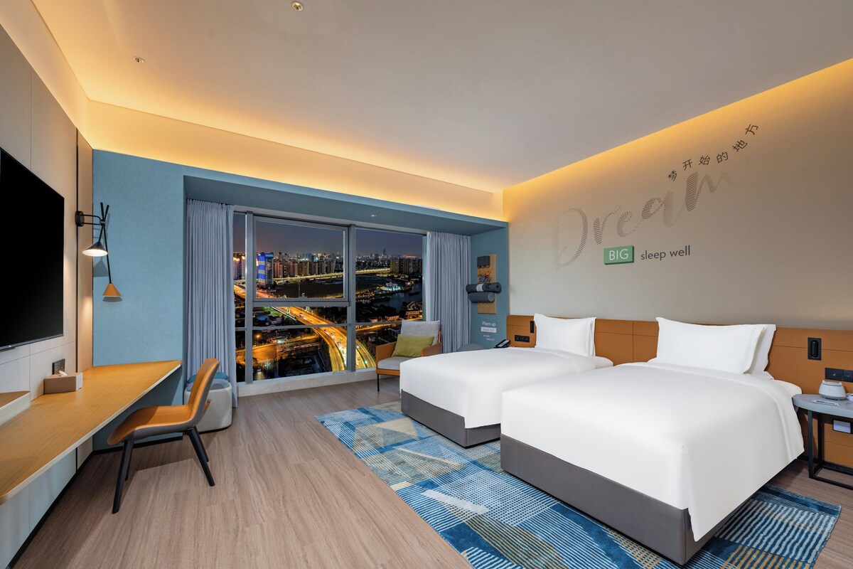 A hotel room with a city view, a desk, and a bed with white linens.