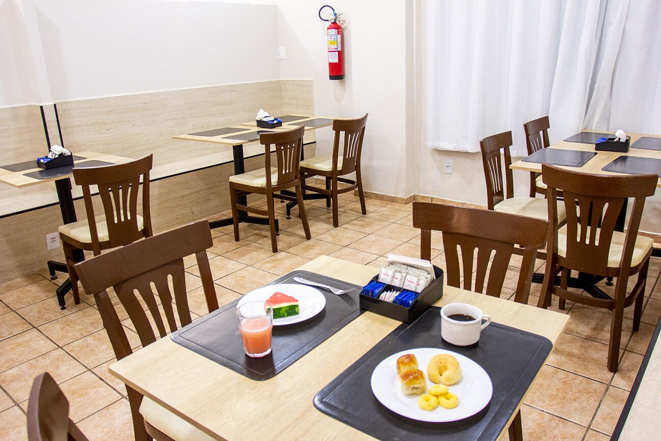 A hotel dining area with multiple tables and chairs, breakfast items, and a fire extinguisher on the wall.