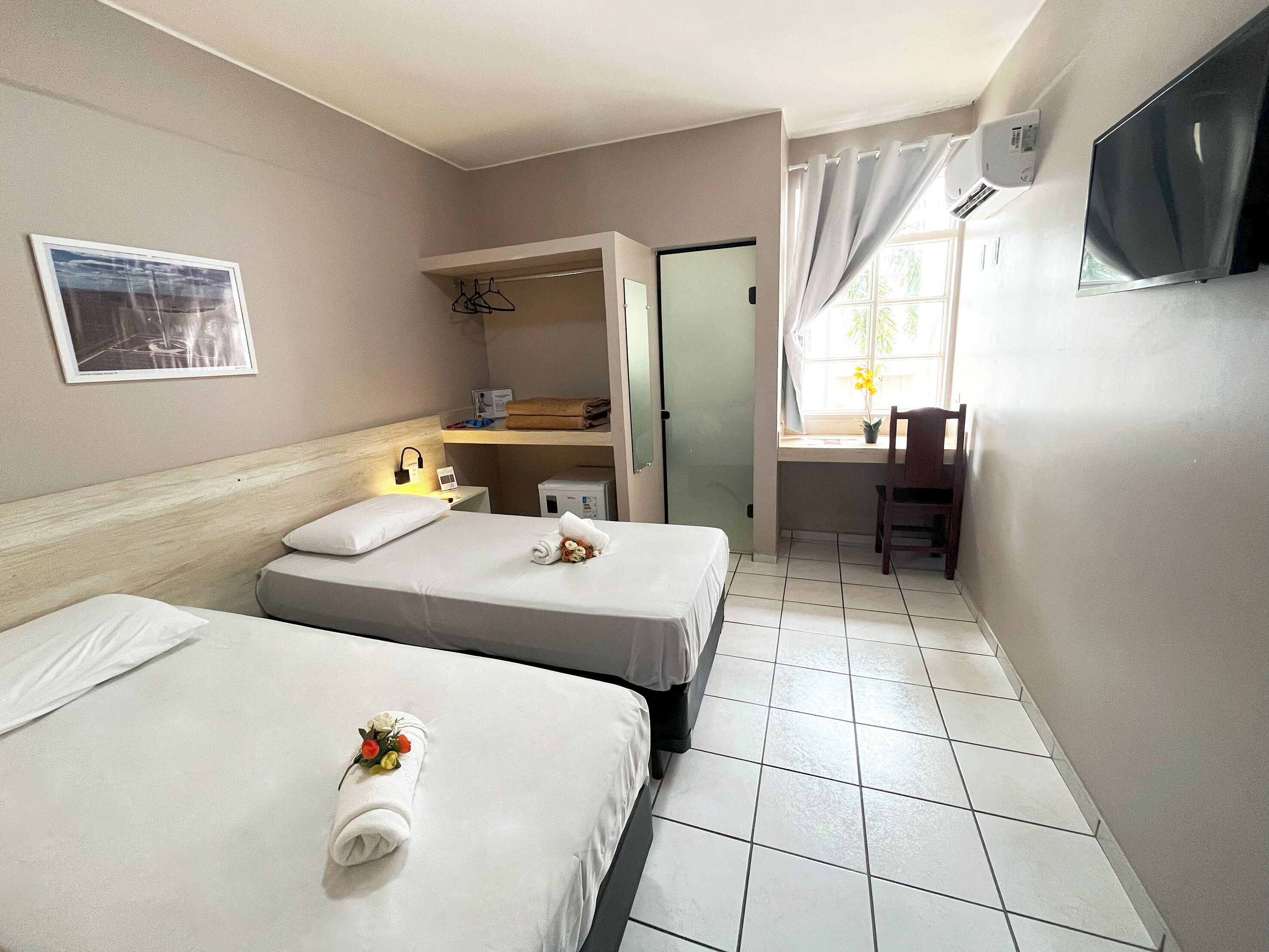 A hotel room with two beds, a desk, a chair, a TV, and a window with curtains.