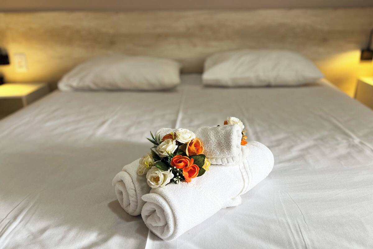 Un lit bien fait, avec du linge de lit blanc et un bouquet de fleurs posé sur le lit.