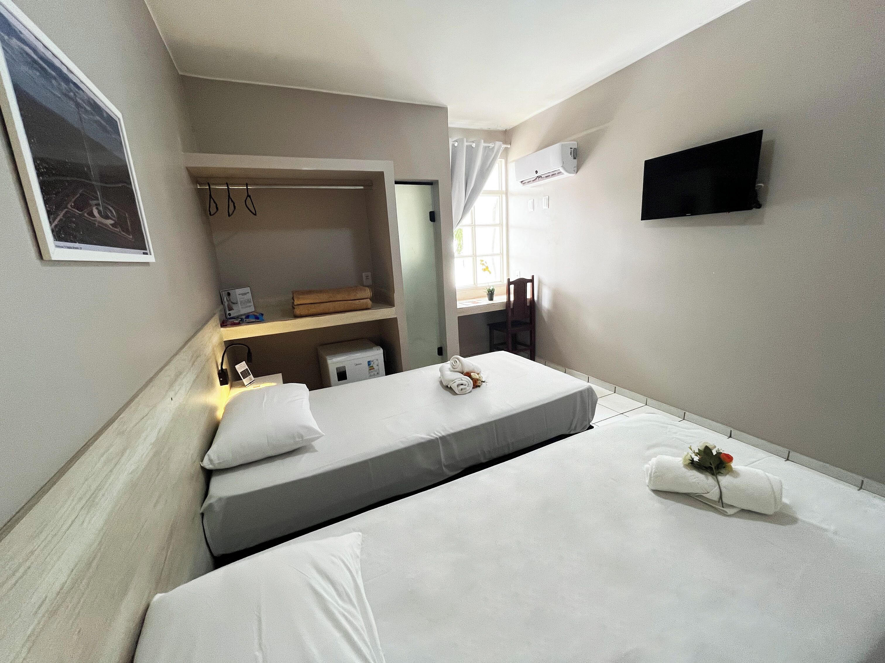 Habitación de hotel con dos camas, un escritorio, una silla, un televisor y una ventana con cortinas.
