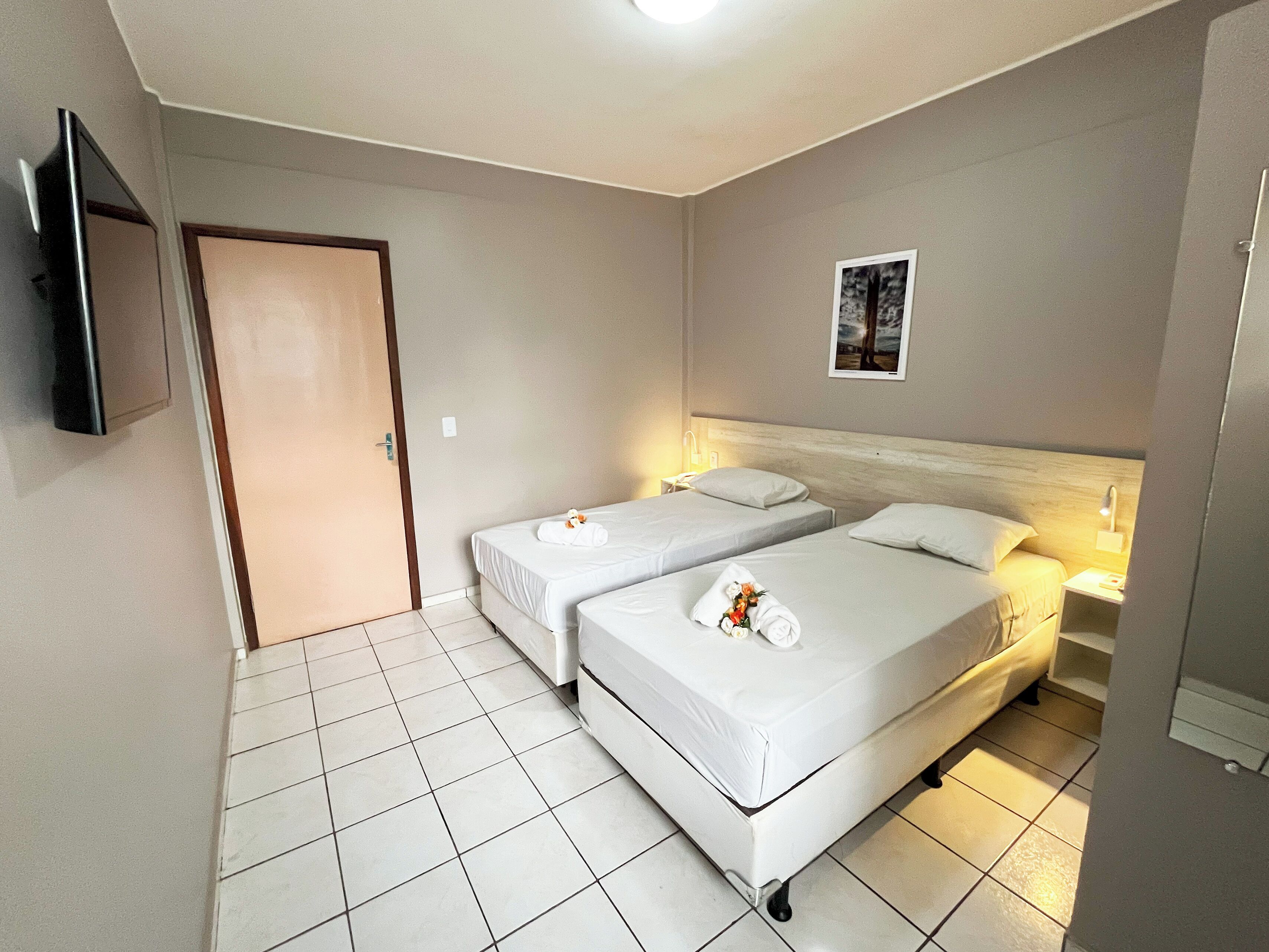 Une chambre d’hôtel avec deux lits simples, un téléviseur à écran plat fixé au mur et une porte.