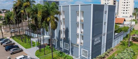 Un hôtel moderne avec un toit plat, de nombreux balcons et un parking rempli de voitures.