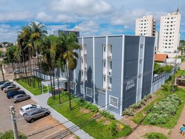 Un moderno edificio de hotel con techo plano, varios balcones y un estacionamiento con coches.