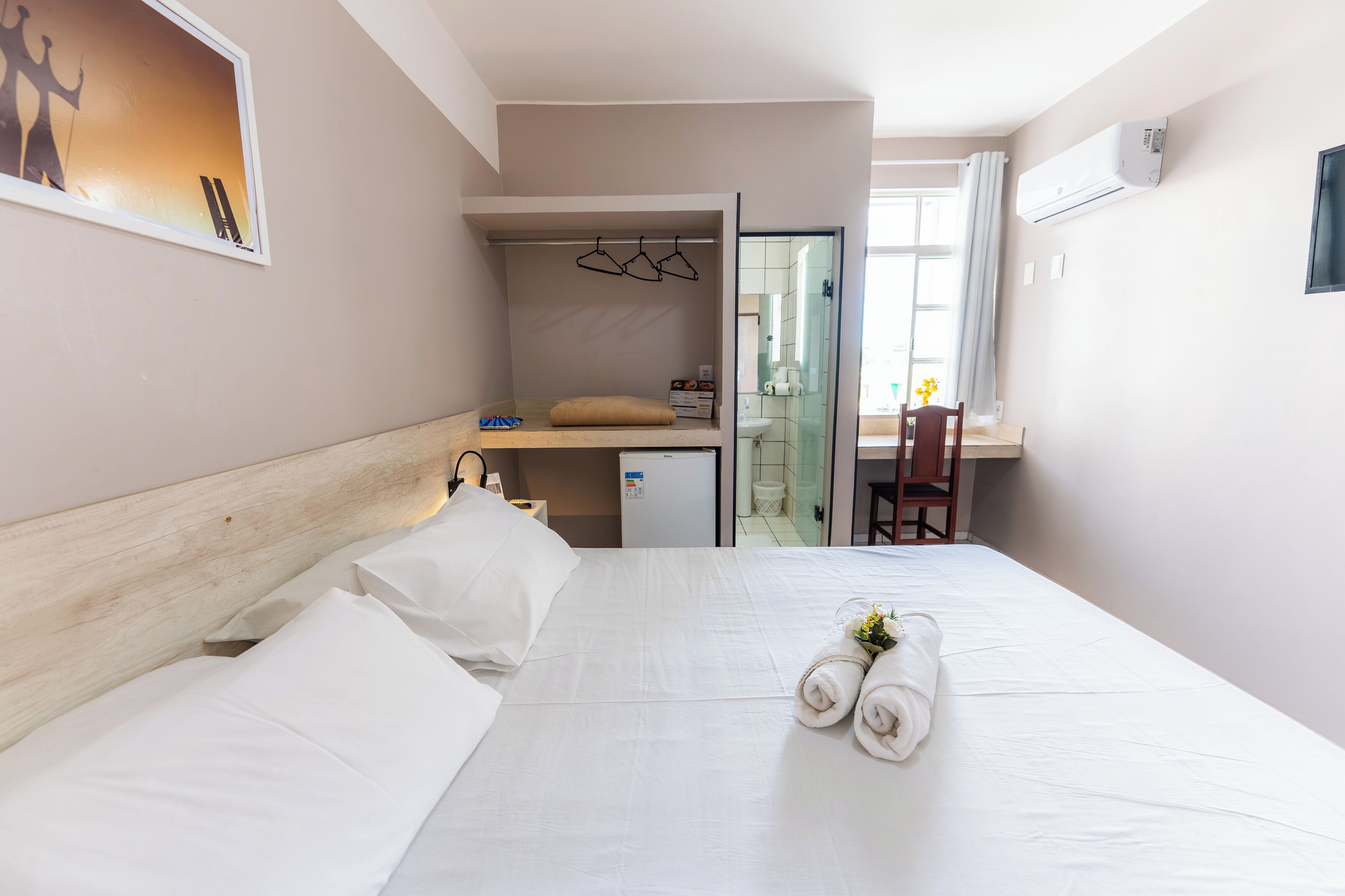 Een hotelkamer met een bed, een bureau, een stoel, een kleine koelkast en een airconditioner.