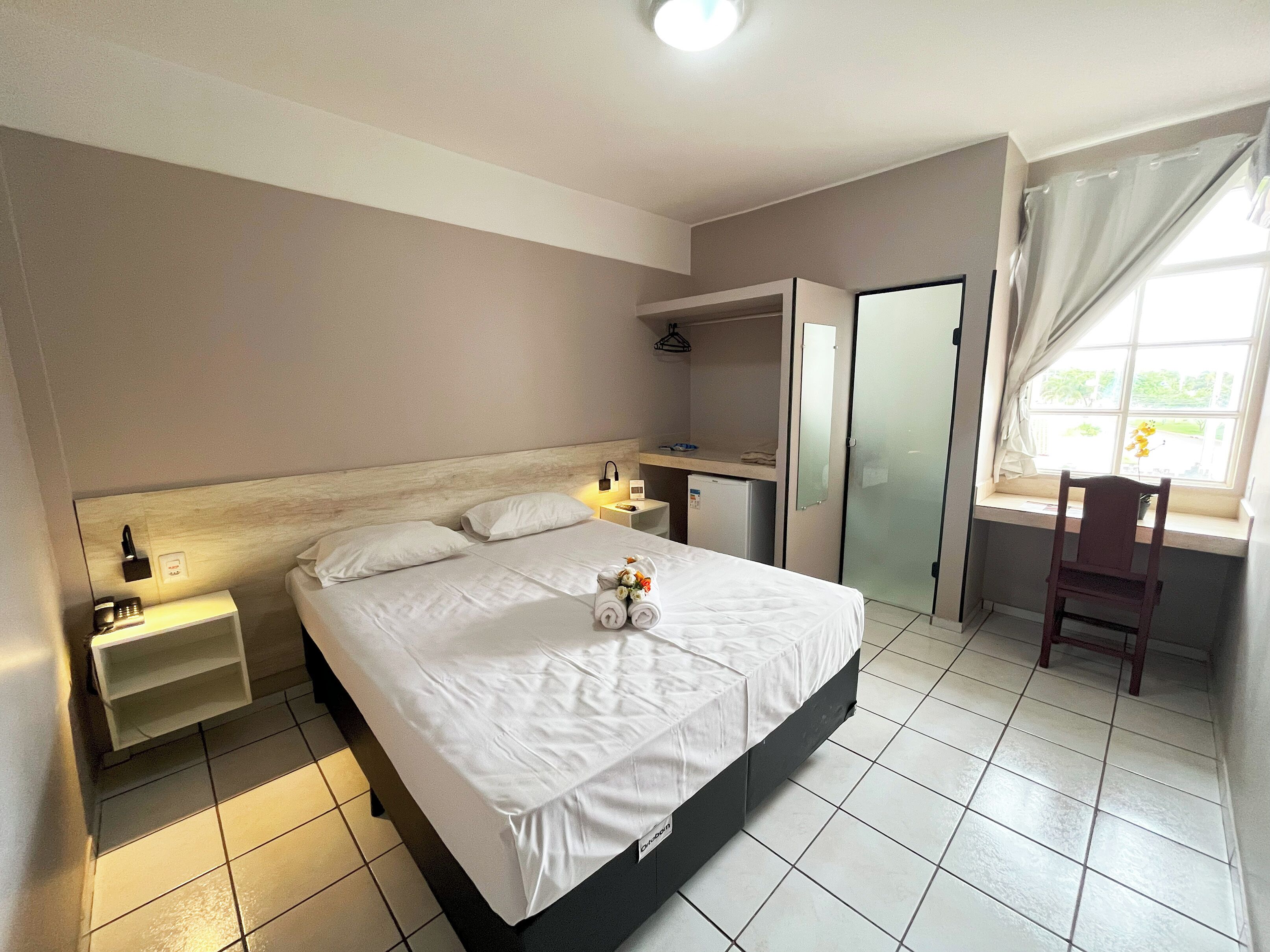 A hotel room with a bed, bedside table, lamp, and a window with curtains.
