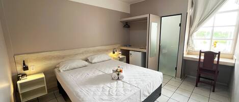 A hotel room with a bed, bedside table, lamp, and a window with curtains.