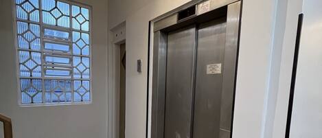 A hallway with an elevator, a window with a geometric pattern, and a tiled floor.