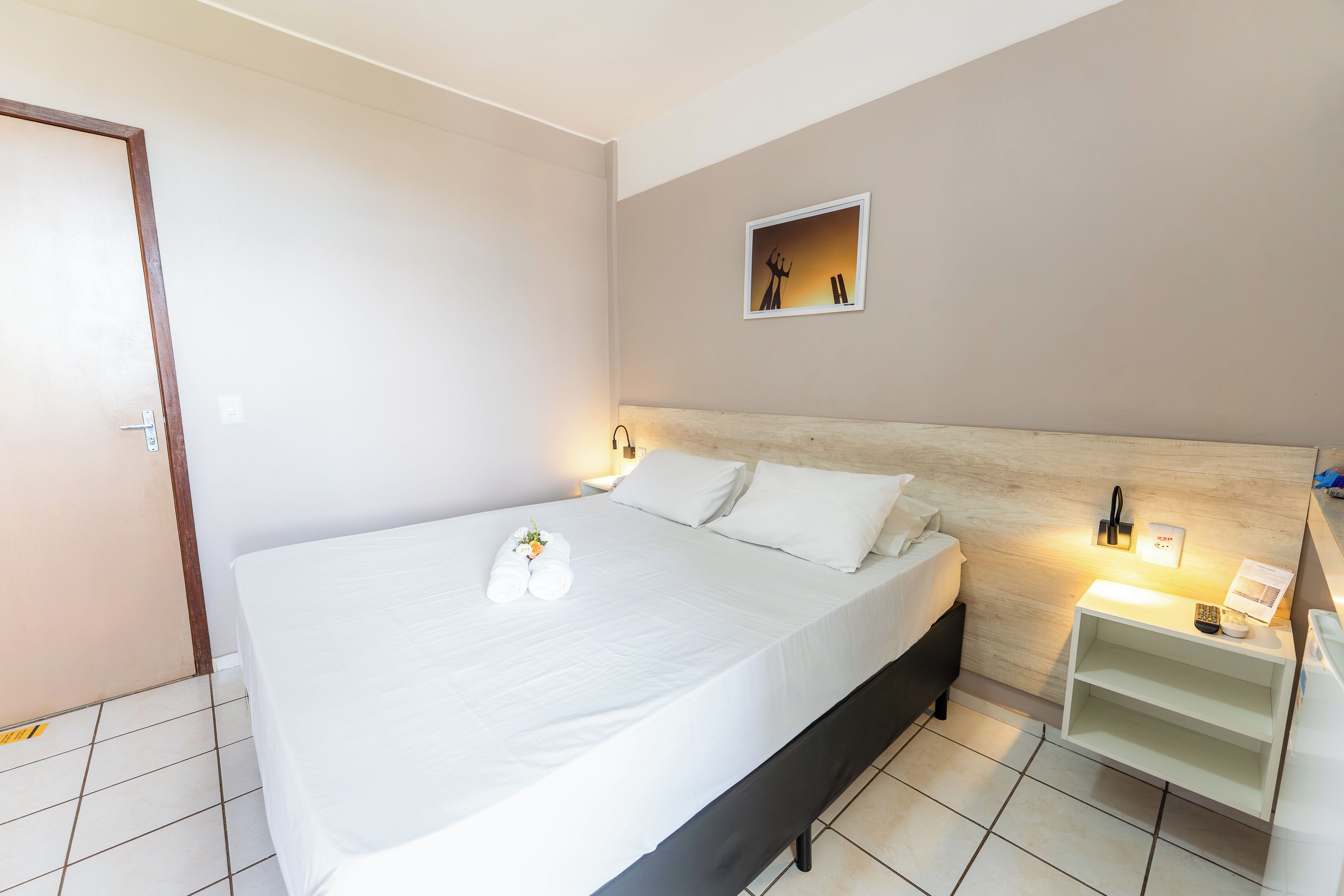 A hotel room with a bed, bedside table, and a small shelf.