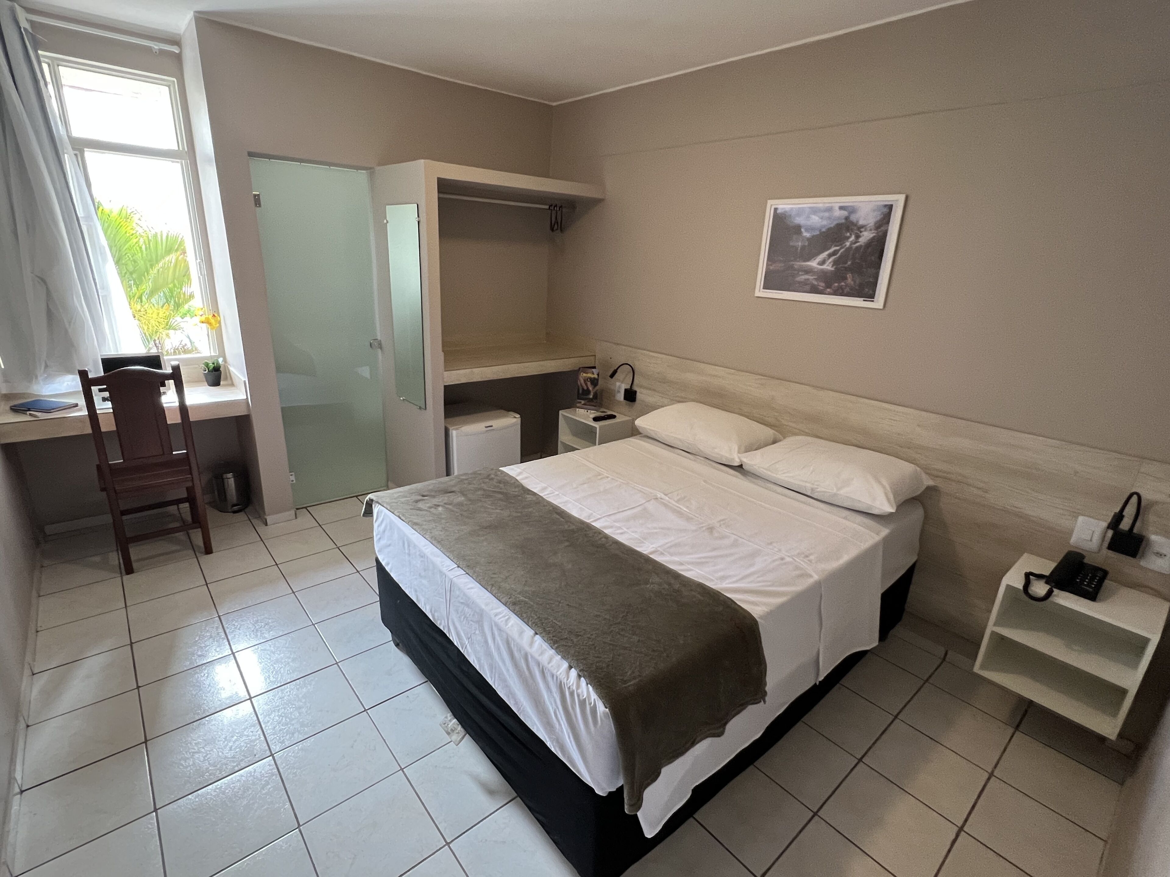 A bedroom with a bed, a desk, a chair, a wardrobe, and a nightstand with a lamp.