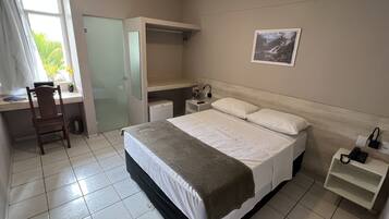 Un dormitorio con cama, escritorio, silla, armario y mesita de noche con lámpara.