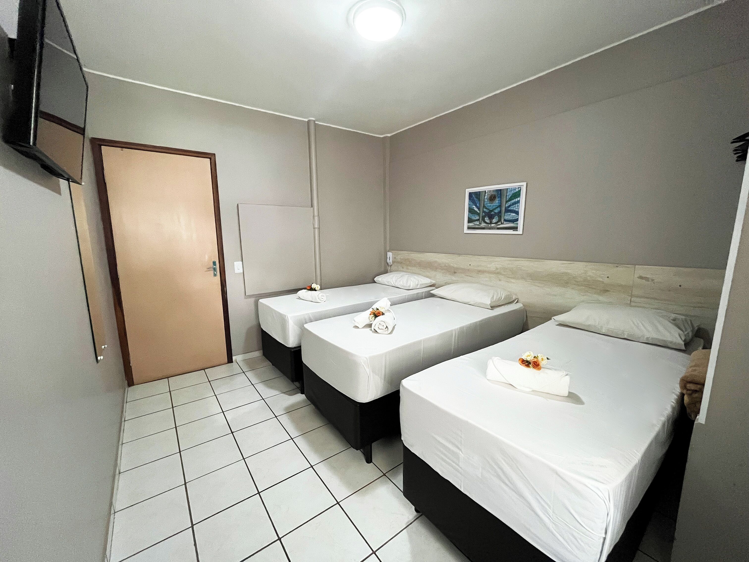 A hotel room with two single beds, a wooden headboard, a flat-screen TV mounted on the wall, and a tiled floor.