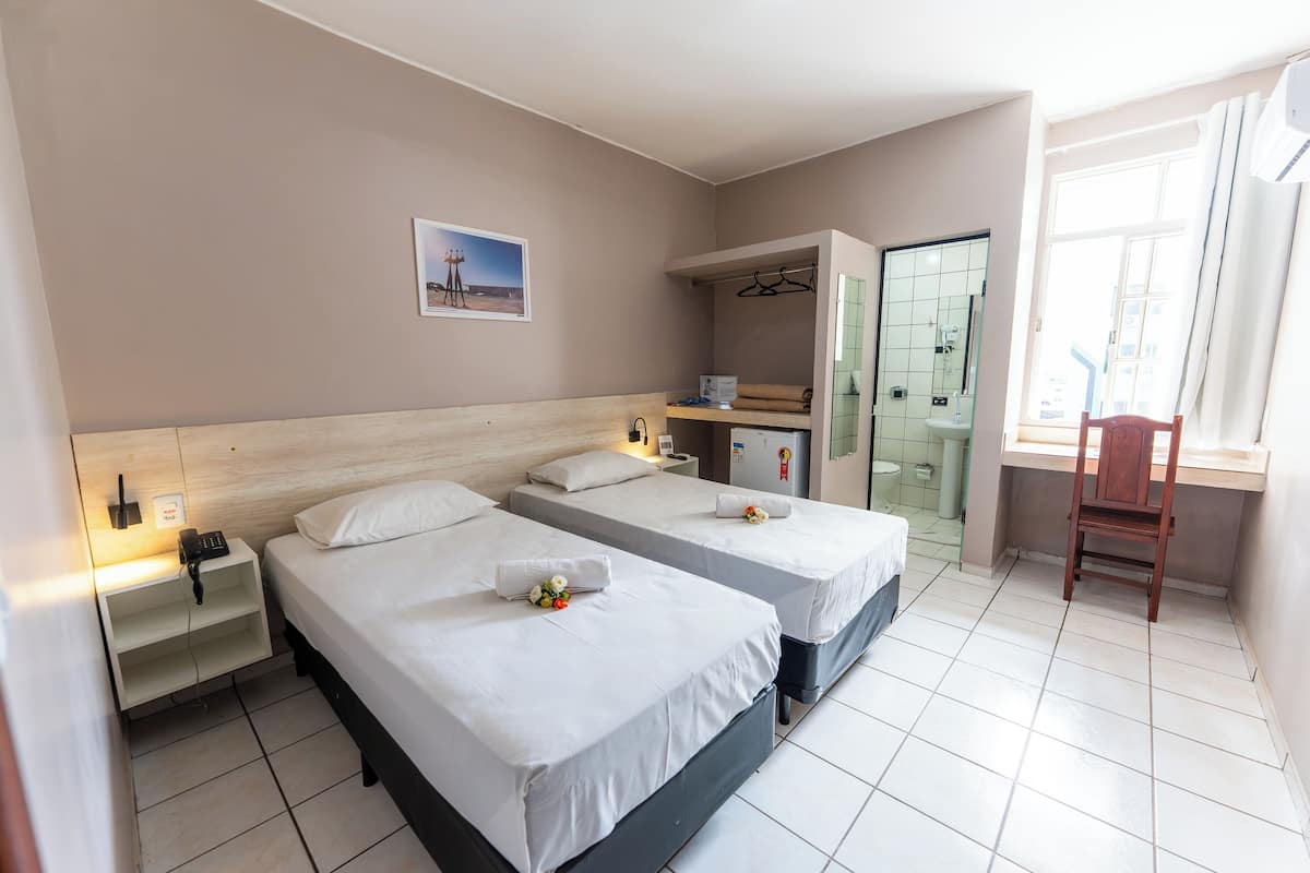 Une chambre d’hôtel avec deux lits, un bureau, une chaise, une salle de bain et une fenêtre.