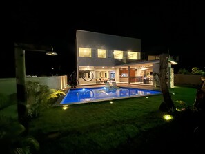 A modern two-story house with a swimming pool, outdoor seating, and a well-lit patio area.
