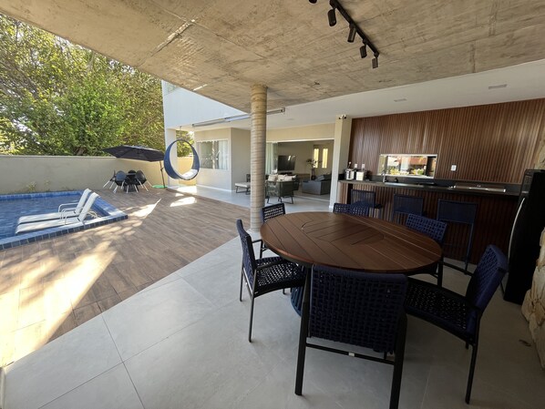 A modern outdoor patio with a pool, dining area, and kitchen.