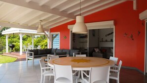 A covered outdoor area with a round table and white chairs, a sofa, and a grill. - Full equiped Villa with swimming pool (Deshaies)