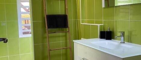 A bathroom with green tiled walls, a white vanity with a mirror, and a wooden ladder leaning against the wall.