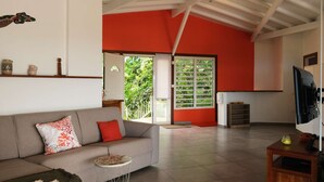 A spacious living area with a grey sofa, a small round table, and a TV on a wooden stand. - Full equiped Villa with swimming pool (Deshaies)
