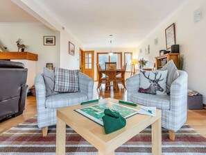 A living room with two sofas, a coffee table, a dining table, and a bookshelf.