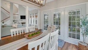 Amplia sala de estar con una mesa de comedor de madera, sillas blancas y una lámpara moderna.