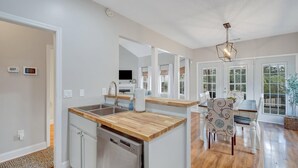 Una cocina moderna con encimera de madera, pileta de acero inoxidable y lavavajillas. Cuenta con una zona de comedor con mesa y sillas, y un amplio ventanal que proporciona luz natural.