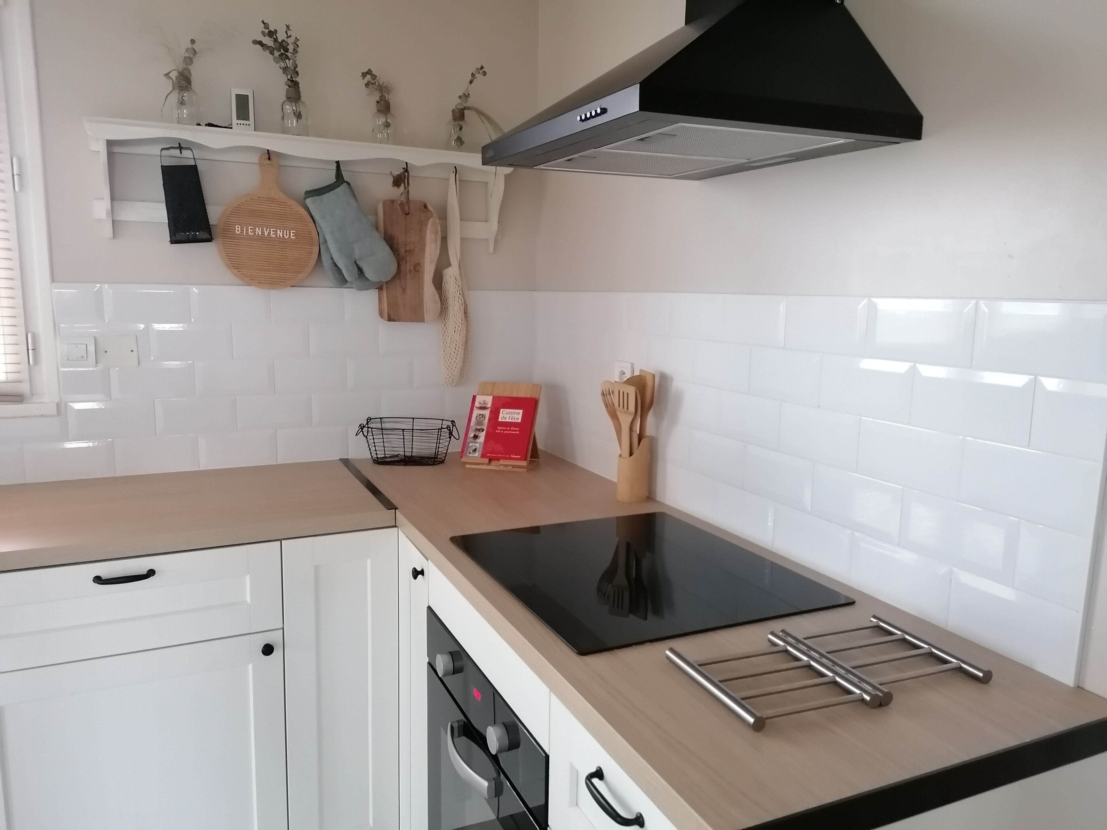 Una cocina moderna con armarios blancos, una placa de inducción negra, un extractor de acero inoxidable y un estante de madera para especias.