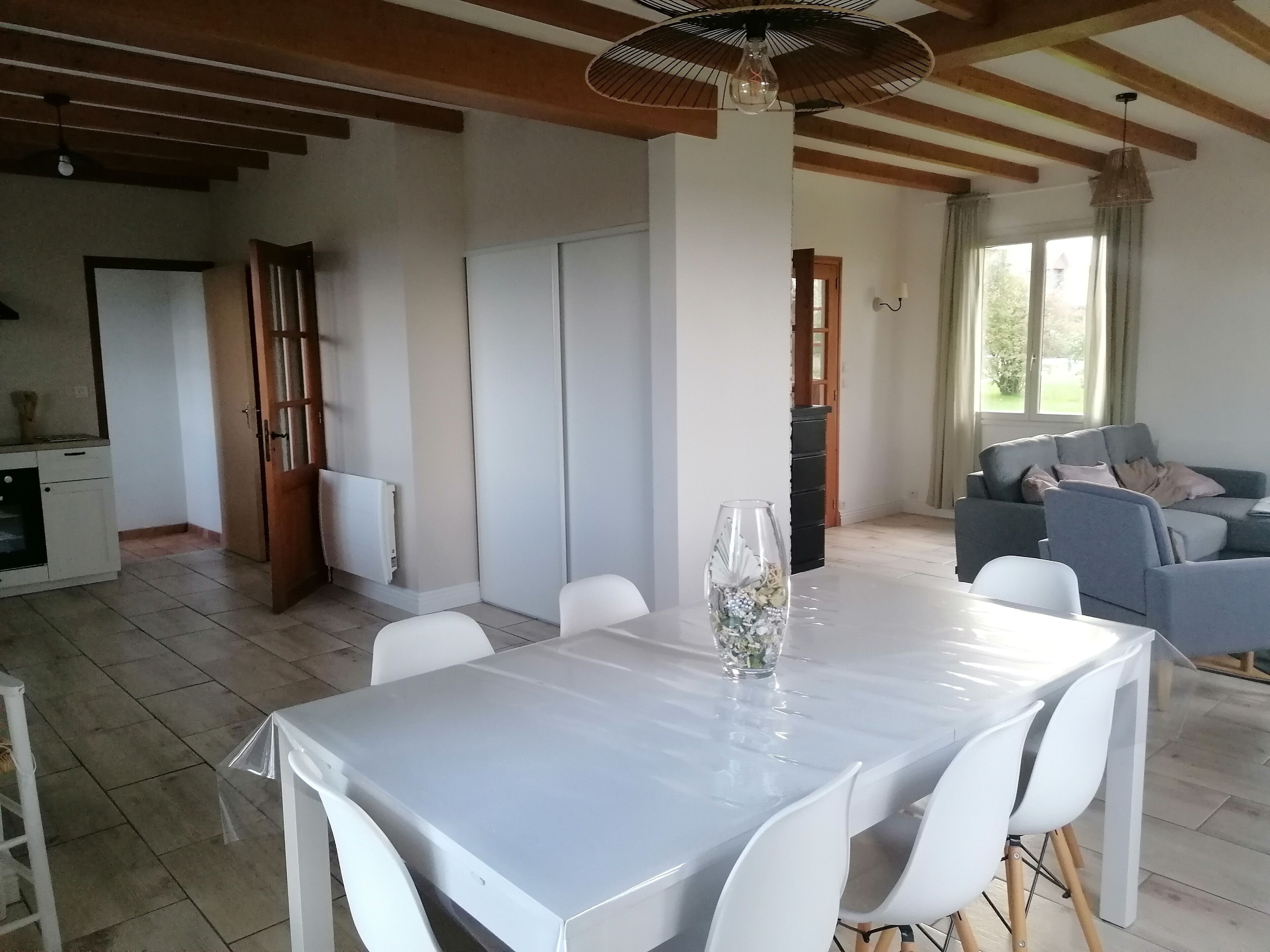 Un'ampia zona giorno con tavolo da pranzo, sedie bianche, divano e una grande finestra.