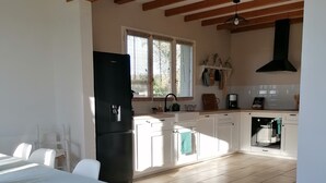 A spacious kitchen with wooden beams, a black refrigerator, white cabinets, and a dining area with a table and chairs.