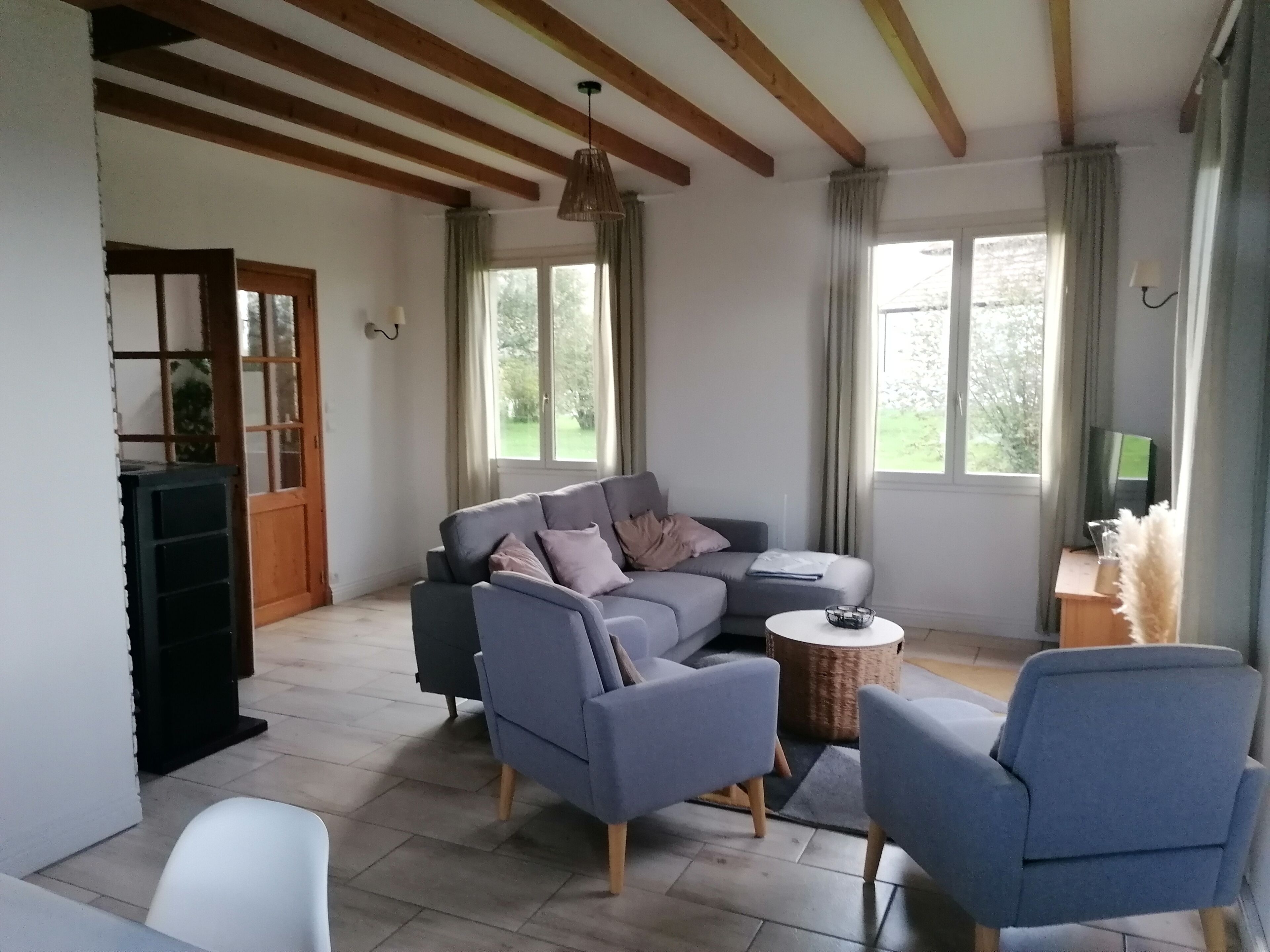 Een moderne woonkamer met een grijze bank, twee fauteuils, een salontafel en een tv op een houten dressoir.