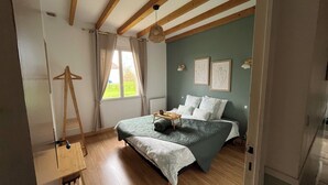 A bedroom with a bed, wooden beams, a hanging light fixture, and a window with curtains.