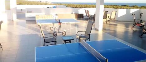 An outdoor table tennis table with chairs, a bicycle, and a view of the sea.