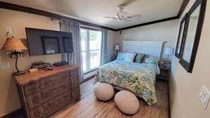 Un dormitorio con cama, cómoda, televisor y ventilador de techo.