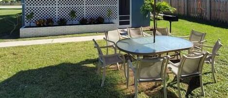 A patio area with a round table and chairs, an orange umbrella, and a white lattice fence.