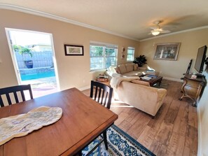 A spacious living room with a dining area, large windows, and a ceiling fan.