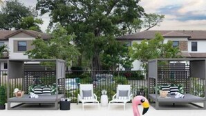 Ein Swimmingpool mit einem rosa Flamingo-Schwimmding, Liegestühlen und einem Zaun, im Hintergrund ist ein Haus zu sehen.