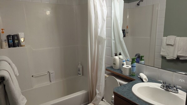 A bathroom with a shower, a sink, and toiletries on the counter.