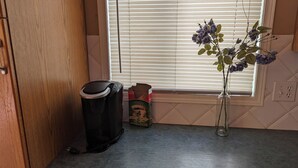 A kitchen with a trash bin, a vase with flowers, and a window with blinds. - 6 beds entire house fenced Yard,  2 car Pad + Garage (3 beds at basement) (Calgary)