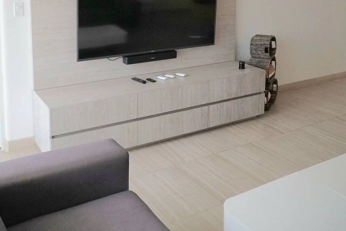 A modern living room with a flat-screen TV mounted on a light wood panel, a ceiling fan, and a small side table with a decorative item.