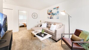 Ein modernes Wohnzimmer mit einem beigen Sofa, einem Couchtisch, einem Fernseher und einem Bild an der Wand.