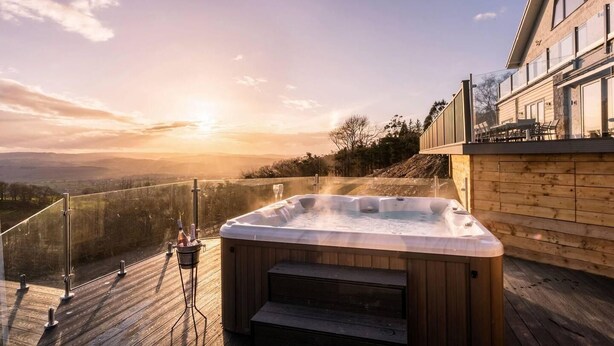 Un bain à remous sur une terrasse en bois, avec vue sur le coucher de soleil et les montagnes.