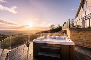 A hot tub on a wooden deck with a view of the sunset and mountains. - Clwyd Gate Manor Pool Sauna Hottub Cave Wales (Ruthin)